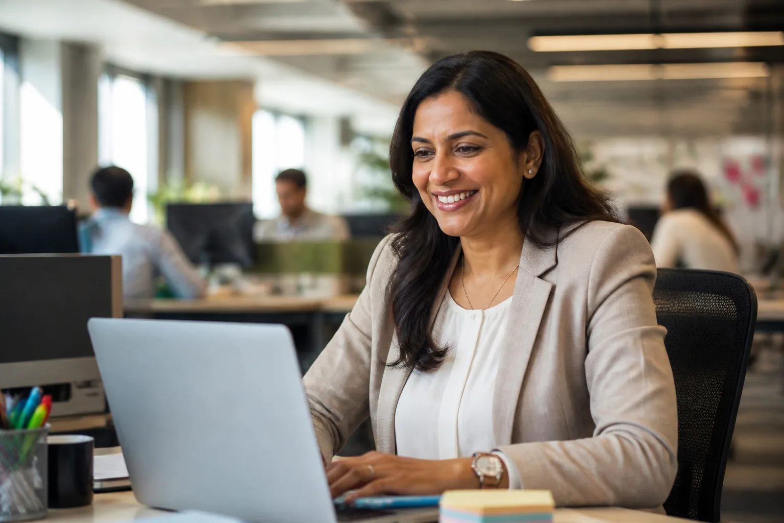 A smiling professional working on a laptop in an open-plan office.